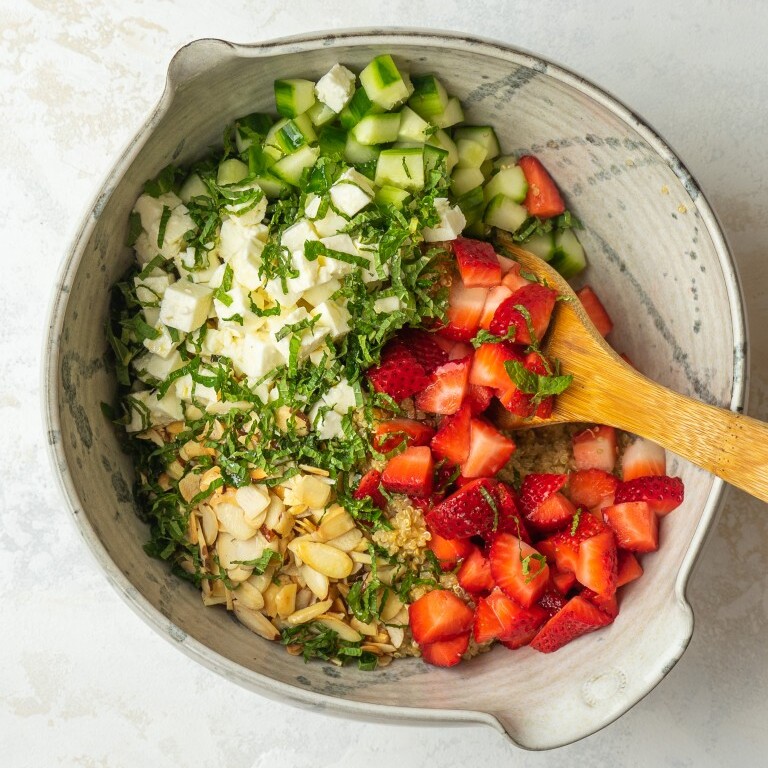 an above view photo of strawberry quinoa salad in a bowl with a wooden spoon