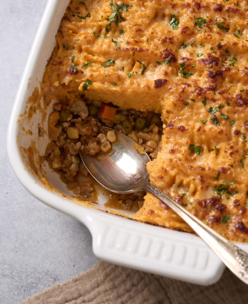 a close up photo of the baking dish with shepherds pie in it with one serving taken out and a spoon resting in the dish