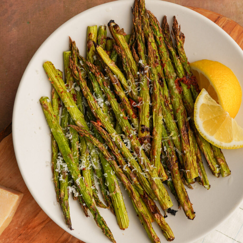 an above view image of air fryer asparagus on a white plate with lemon and parmesan