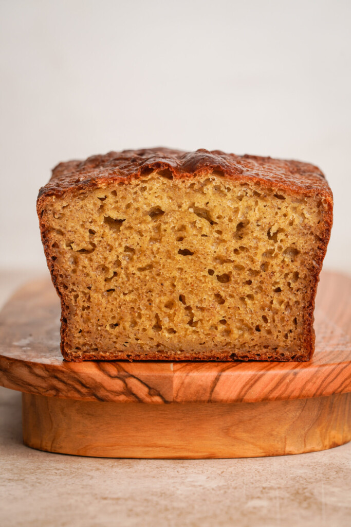 Side view of a loaf of banana bread that has been cut in half on a wooden platform cutting board