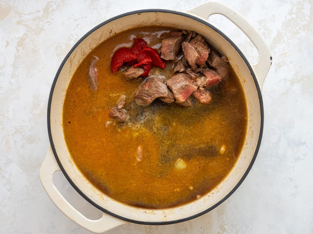 Broth, beer, stew meat, tomato paste and vegetables in a dutch oven