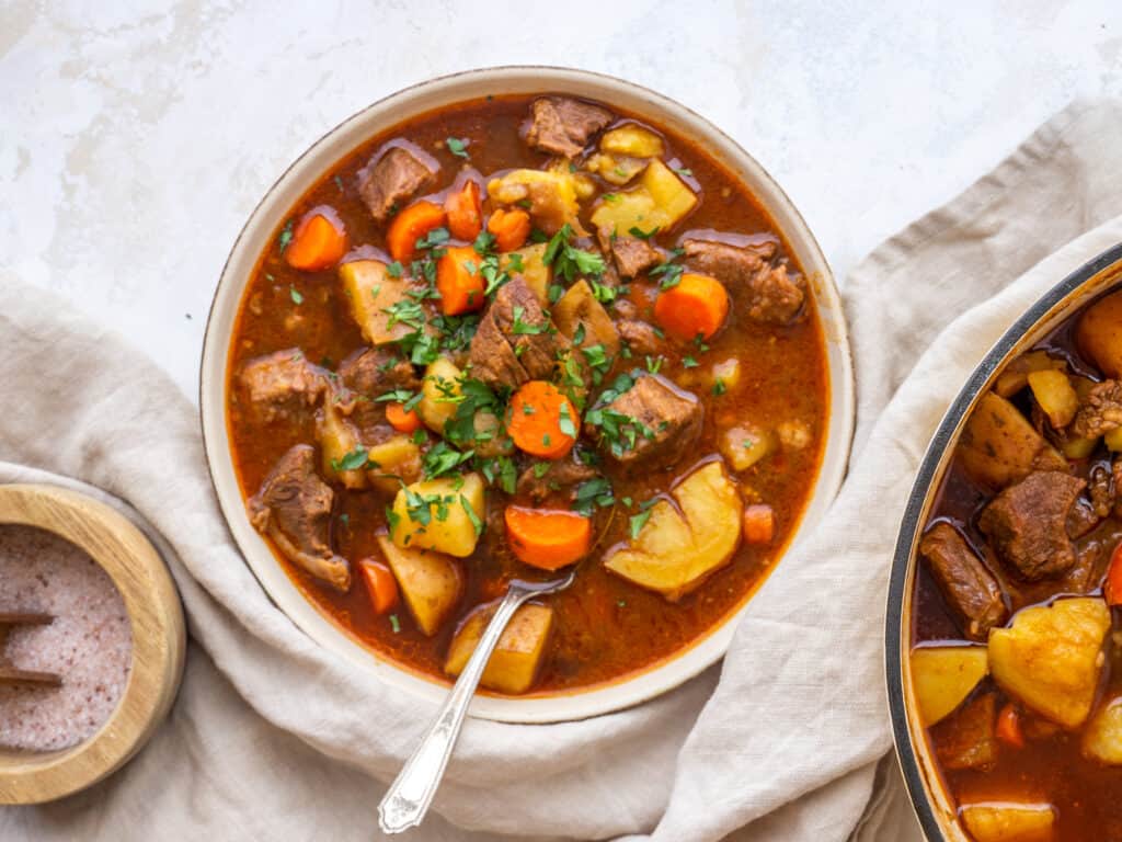 A bowl of rich irish beef stew in a serving bowl with a spoon in the bowl
