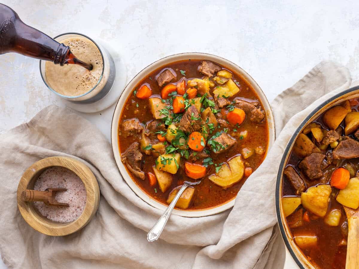 A bowl of cozy irish beef stew with a glass next to it
