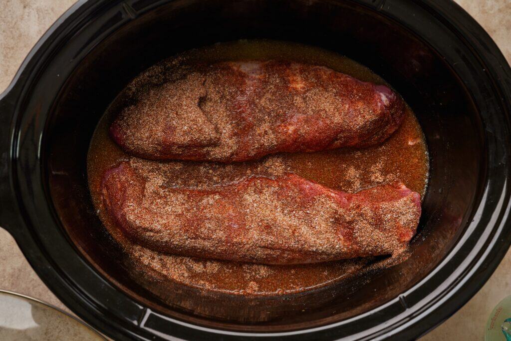 Two pork tenderloins in a slow cooker tossed in a seasoning blend and pineapple juice