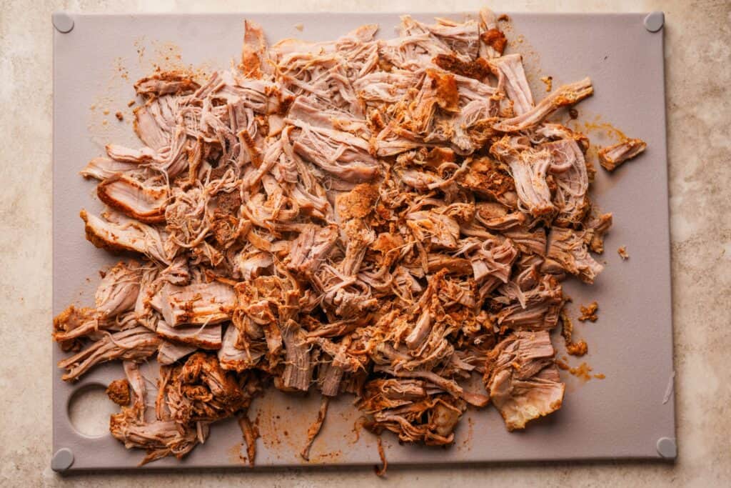 Shredded cooked pork tenderloin on a cutting board