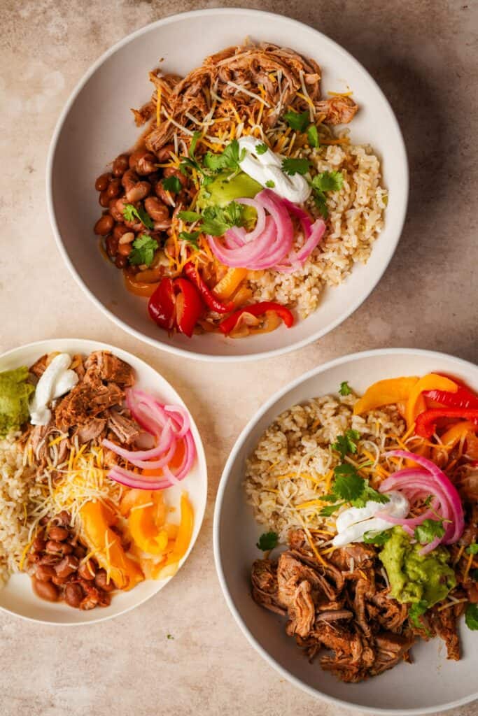 an above view photo of three burrito bowls with slow cooker shredded pork tenderloin