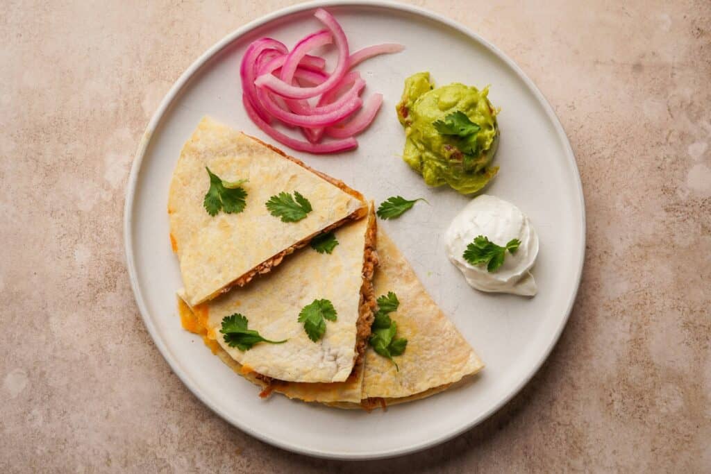 A serving plate with a shredded pork quesadilla nd toppings on it