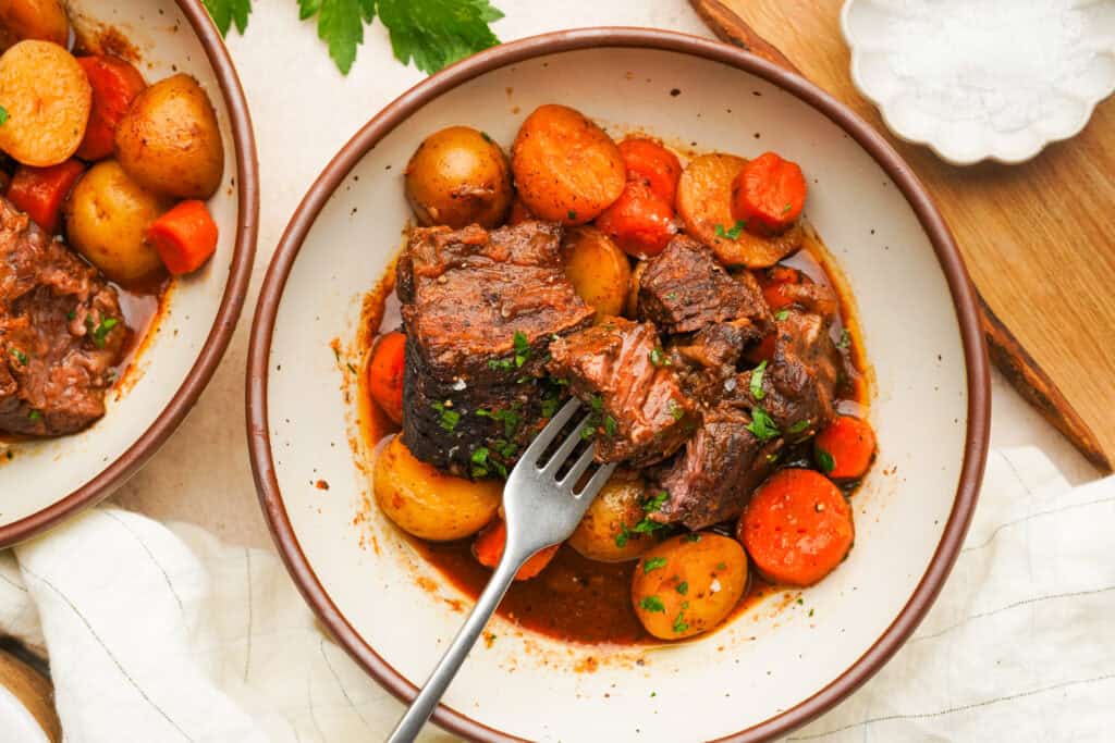 an above view photo of slow cooker short ribs in a bowl with carrots and potatoes with a fork in it