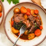 an above view photo of slow cooker short ribs in a bowl with carrots and potatoes with a fork in it