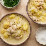an above view image of two bowls of chicken leek soup with salt and parsley in small bowls around it