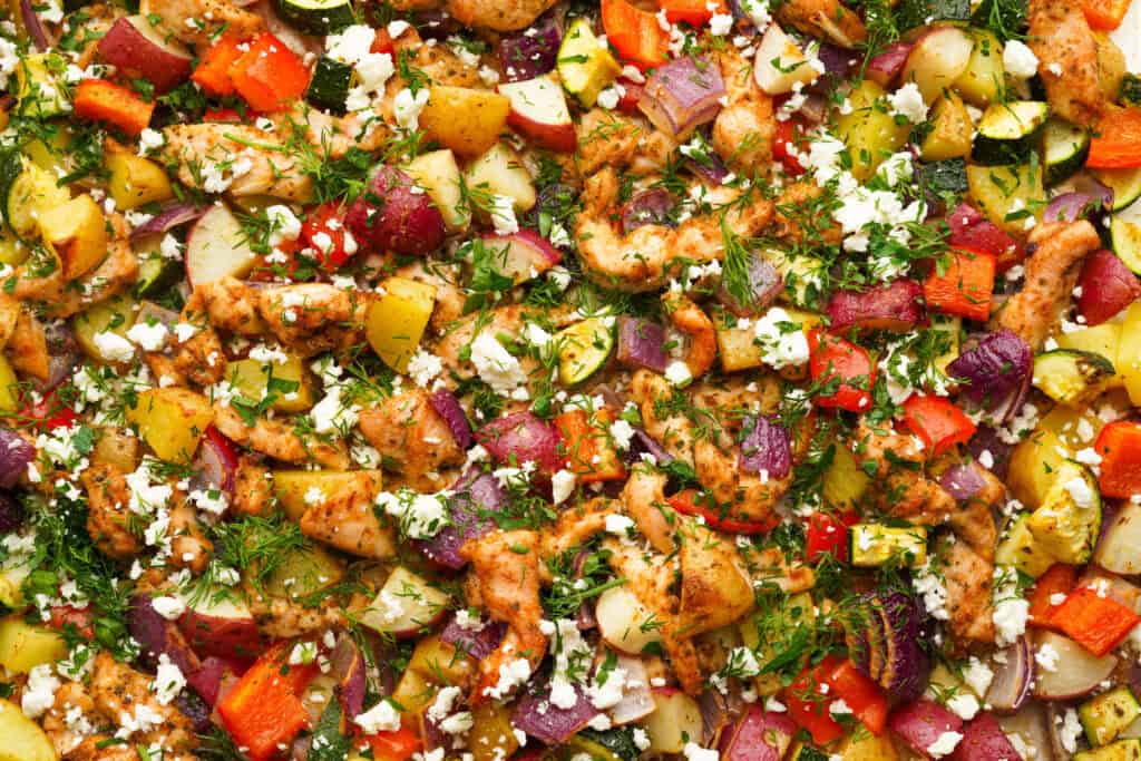 an above view photo of greek sheet pan chicken and veggies on a sheet pan