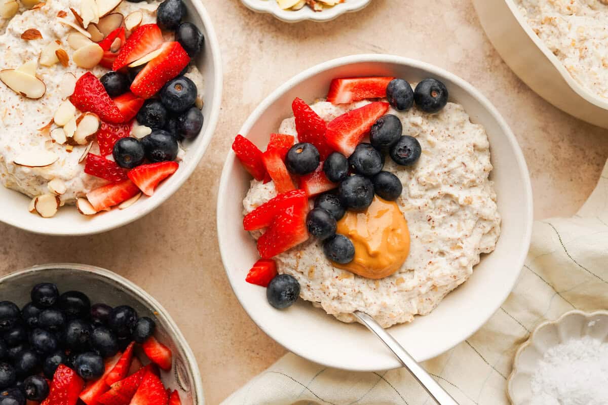 an above view photo of three bowls of protein oatmeal with berries and peanut butter