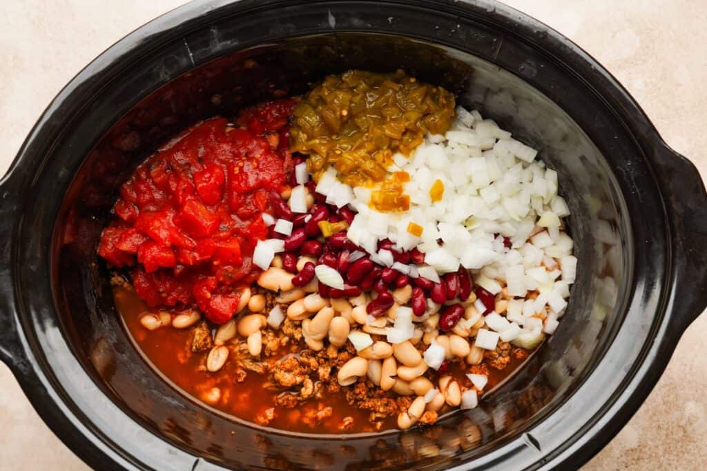 Browned meat, diced onion, diced tomatoes, beans, green chiles, and chicken broth in a slow cooker