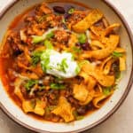 Close up above view of a bowl of slow cooker turkey chili with toppings like corn chips, sour cream, cheese and green onion on top