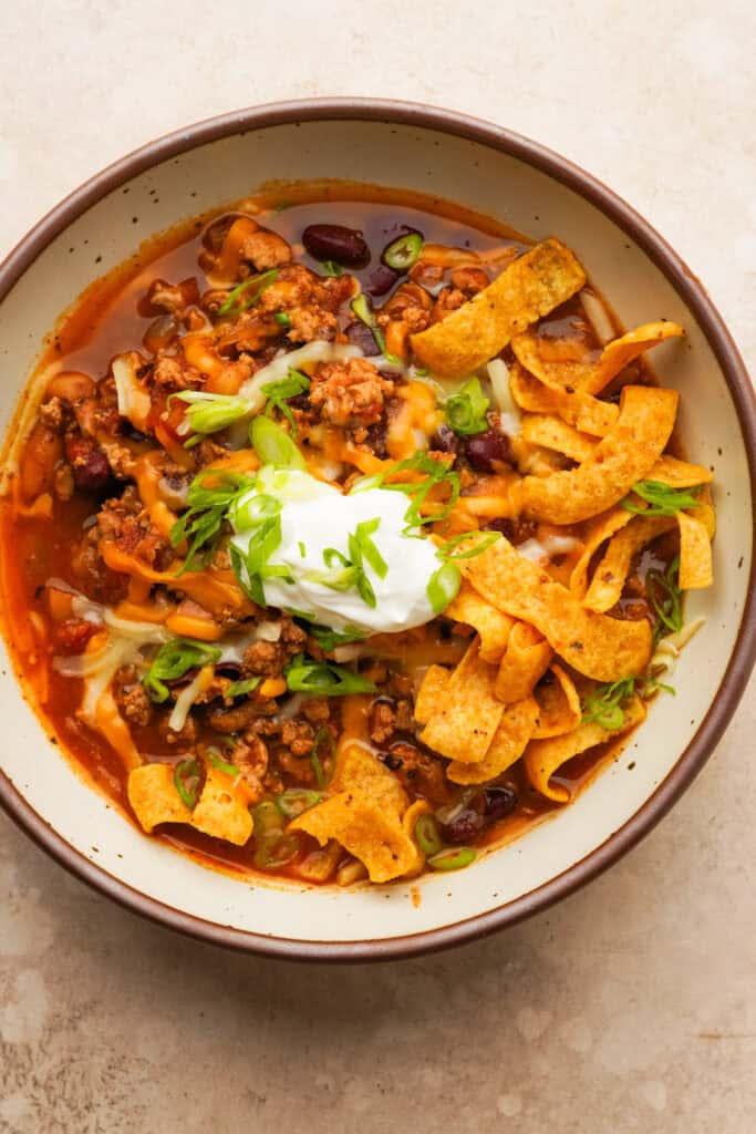 Close up above view of a bowl of slow cooker turkey chili with toppings like corn chips, sour cream, cheese and green onion on top