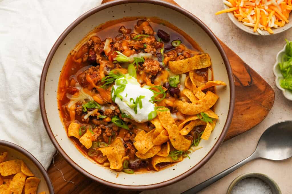 Close up above view of a bowl of slow cooker turkey chili with toppings like corn chips, sour cream, cheese and green onion on top