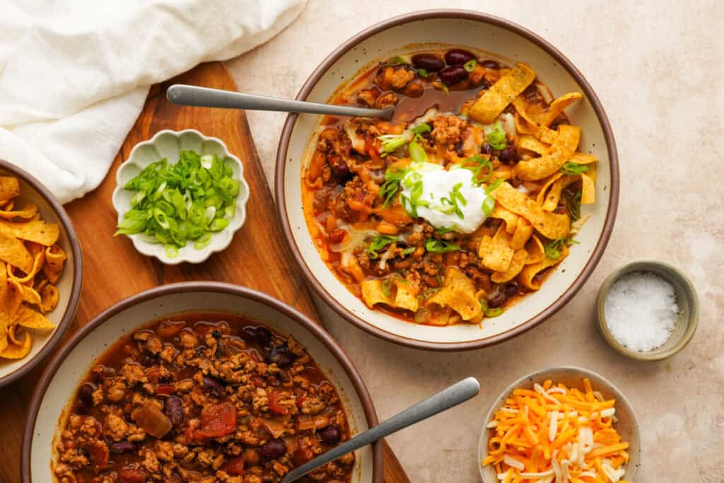 Above view of two bowls of crockpot turkey chili one with toppings on top and one without toppings