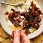 Close up above view of a hand holding a cracker with bacon wrapped date dip on it.