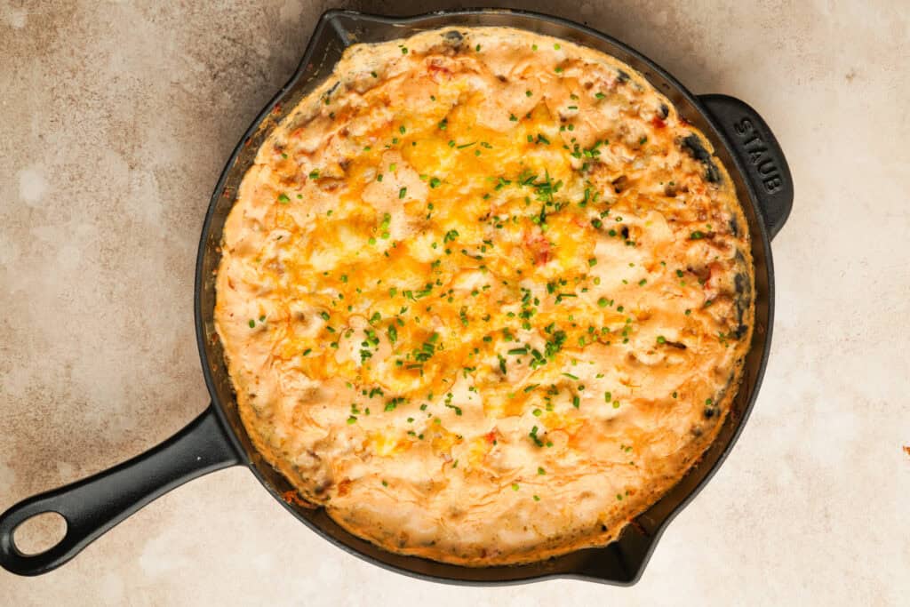 Cheesy baked sausage dip in a cast iron skillet with chives on top