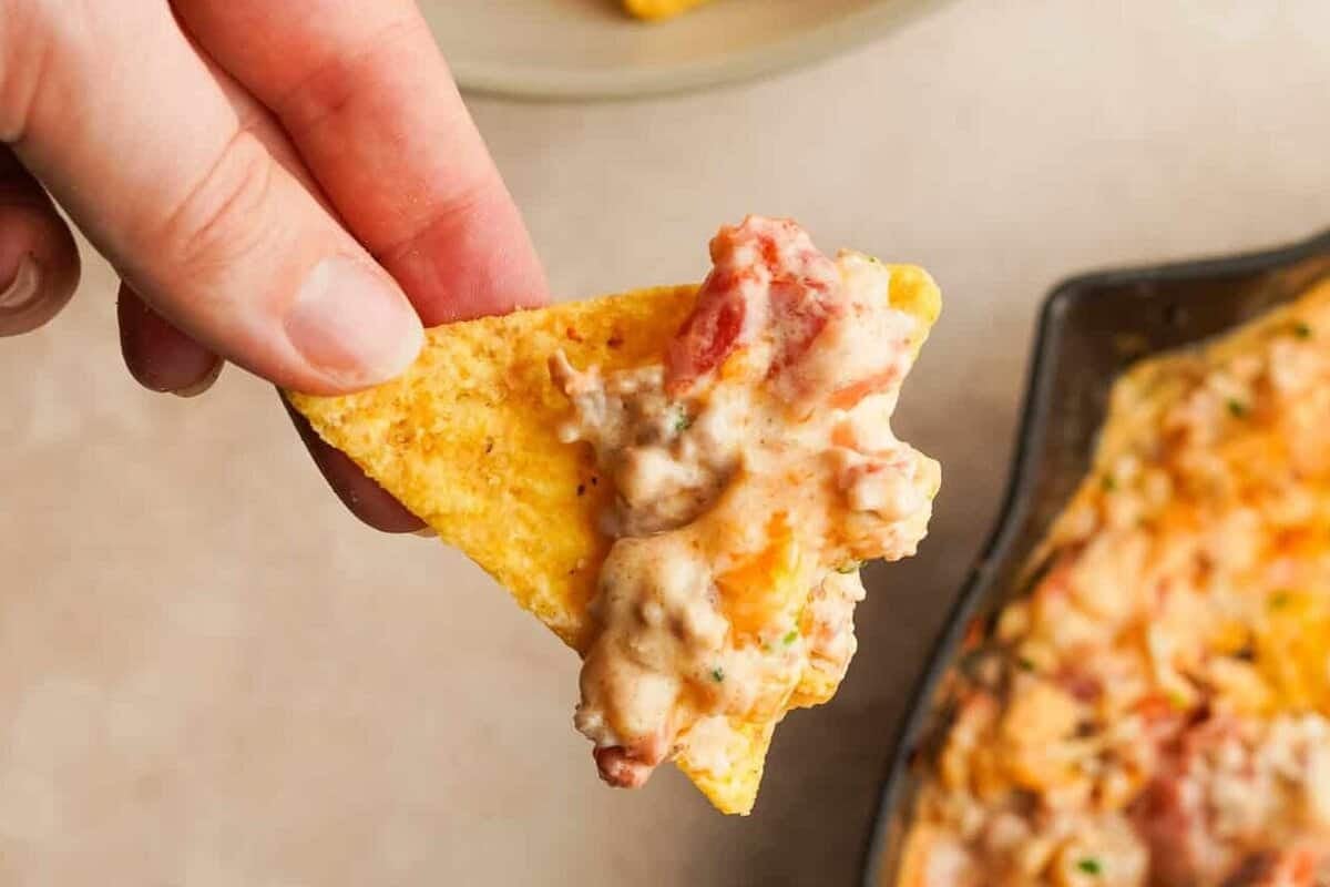 A hand holding a tortilla chip that has cheesy sausage rotel dip on it