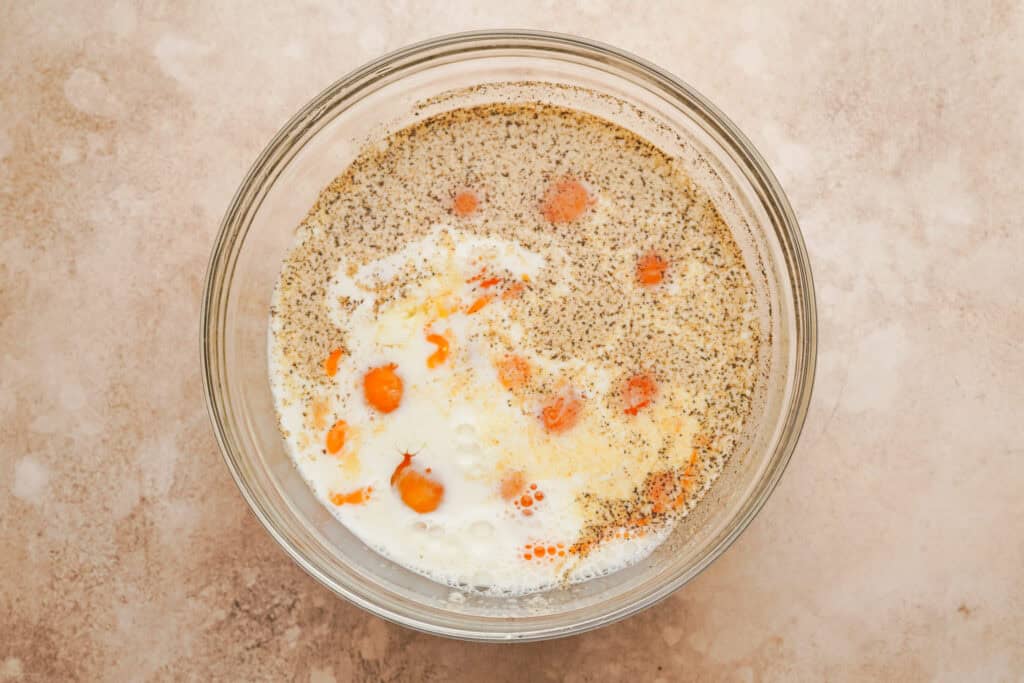 A glass mixing bowl filled with eggs, milk, and spices