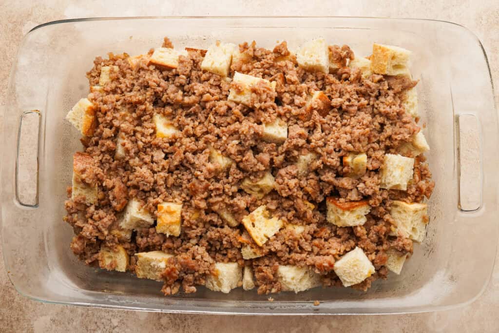 A casserole pan filled with cubed bread and crumbled breakfast sausage
