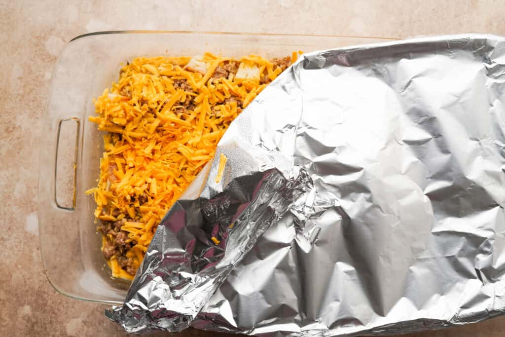 A casserole dish with a prepared but not baked breakfast casserole inside. There is a piece of aluminum foil over top of the casserole