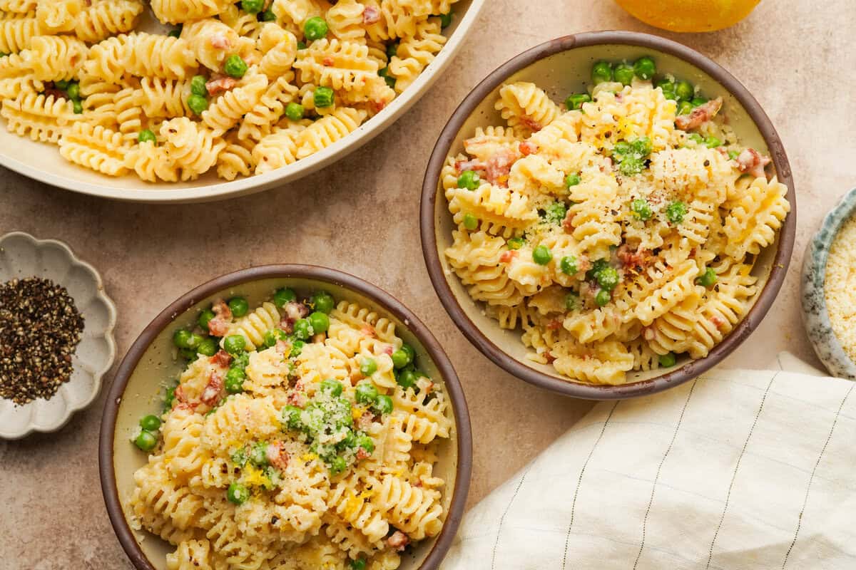 an above view photo of pasta with pancetta and peas in two bowls with a pan of pasta next to them