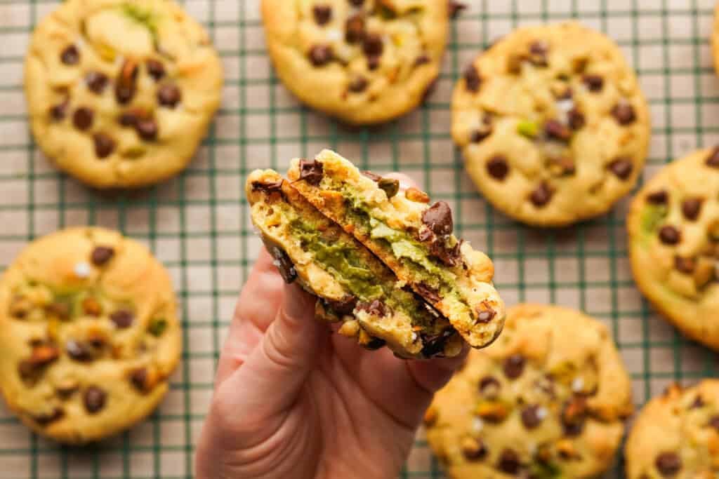 Above view of a hand holding a pistachio cookie that is brown in half showing the pistachio cream filling