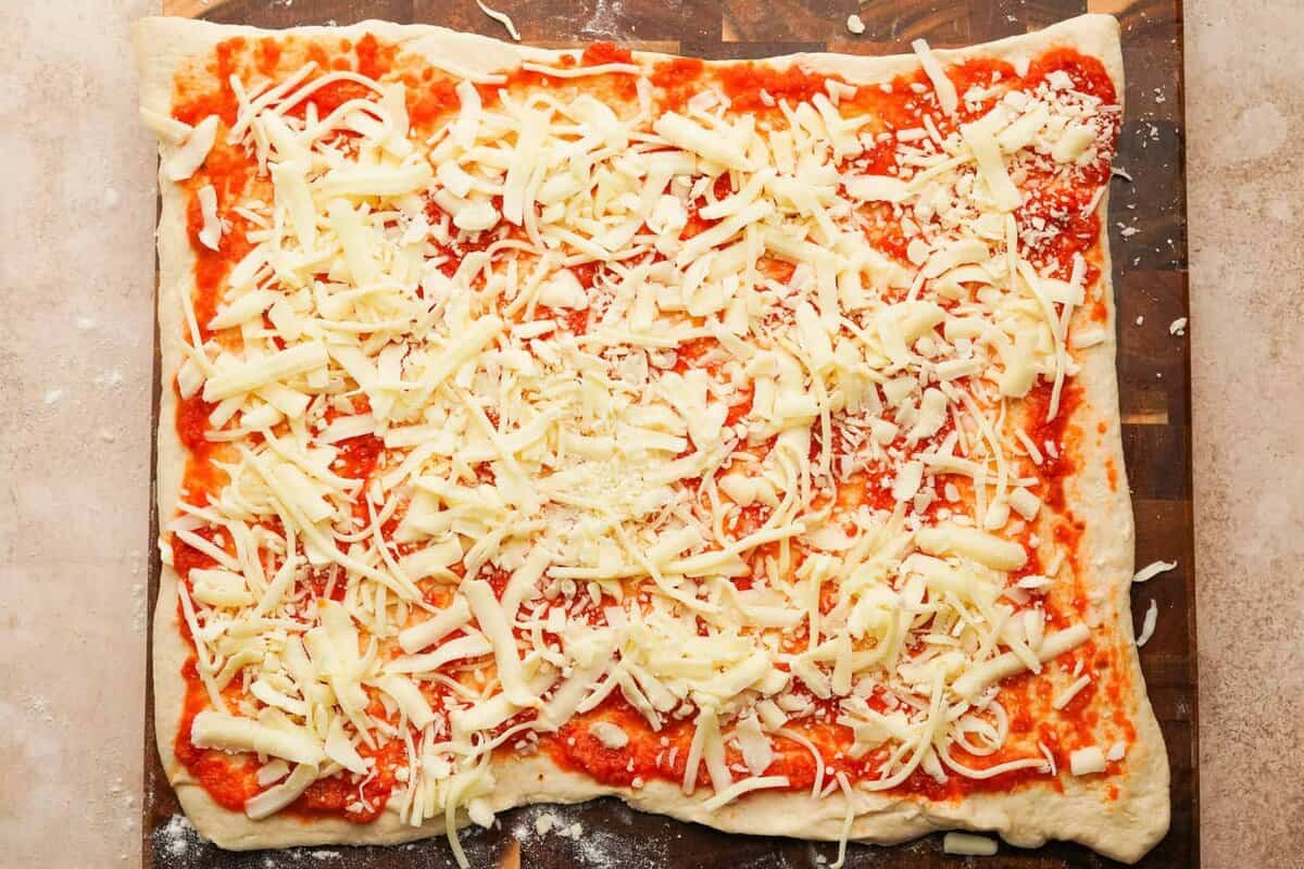 pizza dough with sauce and shredded mozzarella on top on a wooden cutting board