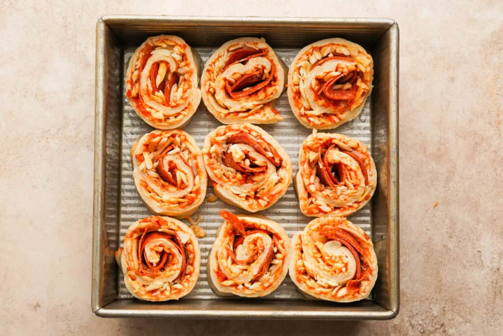 nine unbaked pizza pinwheels in a baking pan