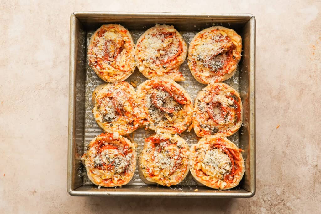 nine pizza pinwheels in a baking pan with parmesan on top