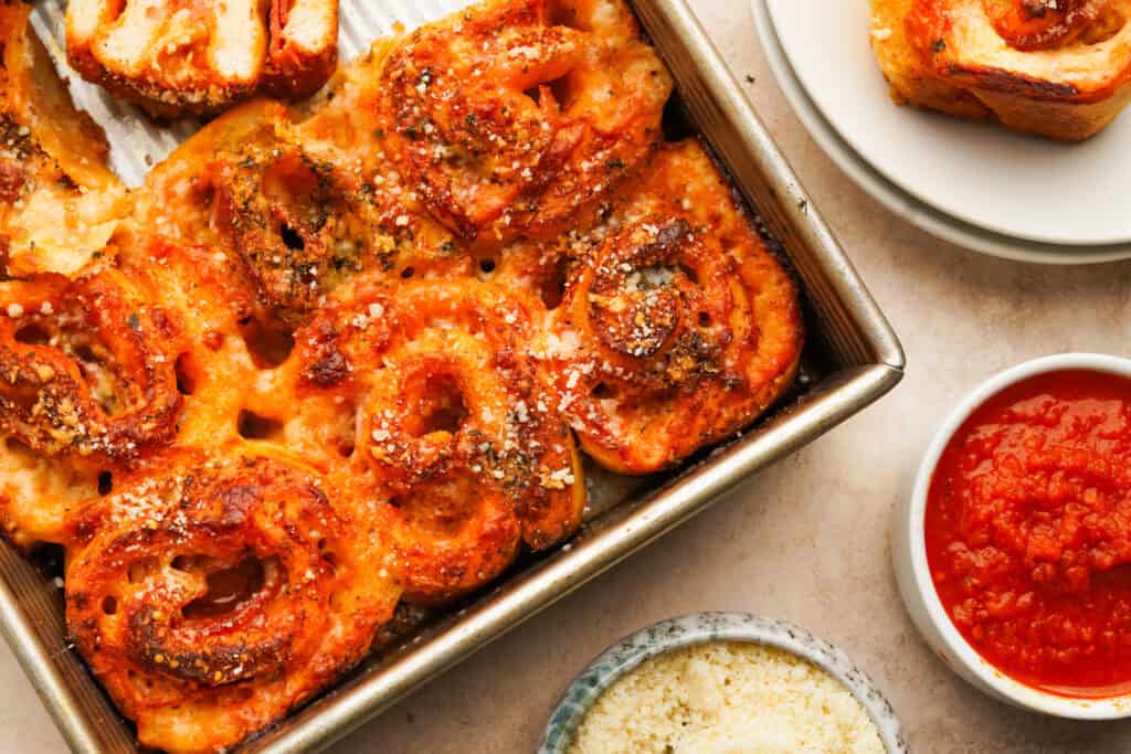 an above view photo of pizza pinwheels in a pan with small bowls of sauce and parmesan next to them