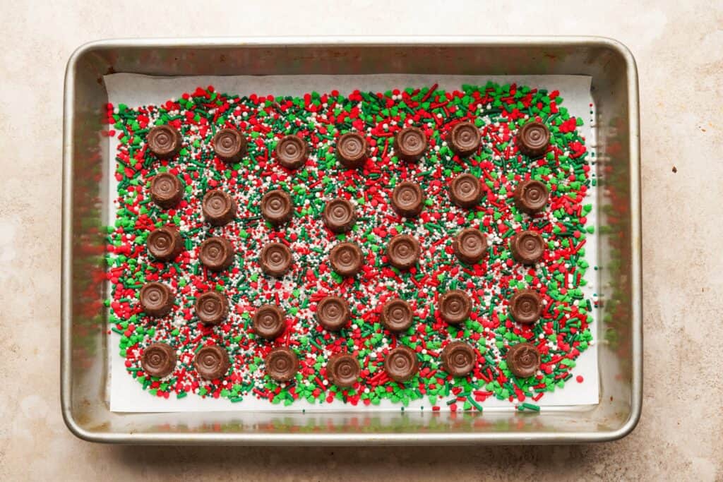 A baking pan filled with a layer of sprinkles, then a layer of rolos with the wrapper off