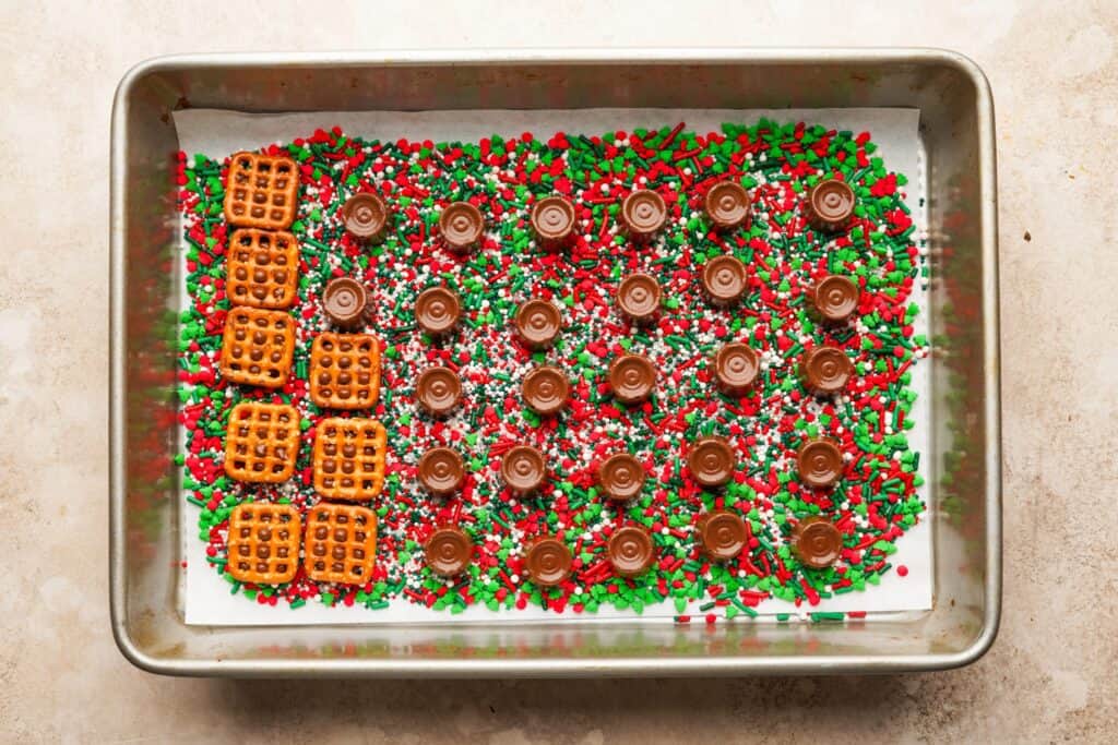 A baking pan filled with a layer of sprinkles, then a layer of rolos, then a few pretzels on some of the rolos. The rolos look warm and melted from the oven