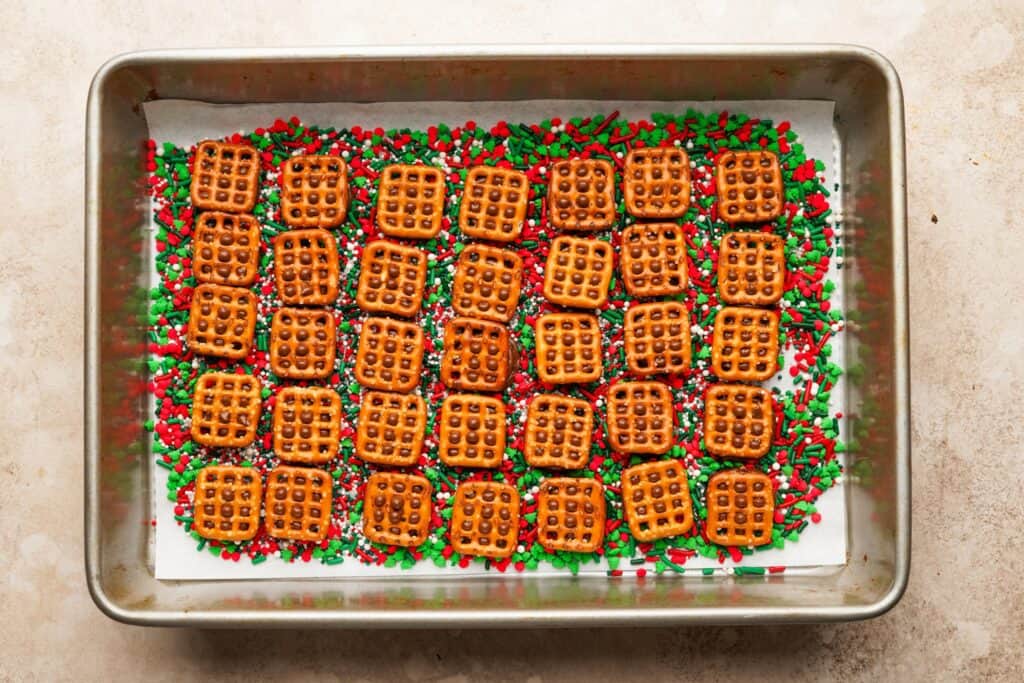 A baking pan filled with a layer of sprinkles, then a layer of rolos, then pretzels on top.