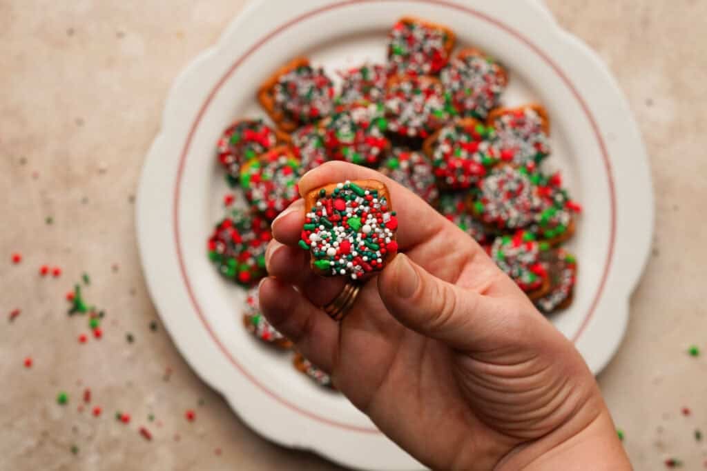 Hand holding a pretzel bite over top of a plate full of pretzel bites