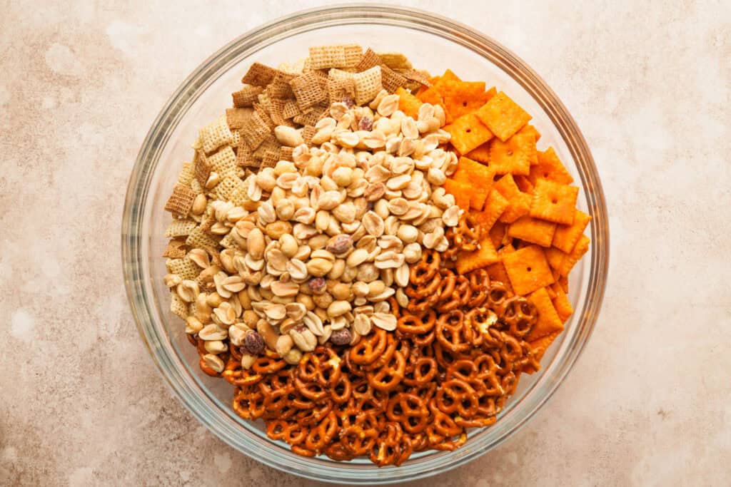 large glass bowl filled with the dry ingredients like chex cereal, pretzels, cheez its and peanuts