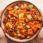 two hands wrapped around serving bowl filled with sweet and salty chex mix