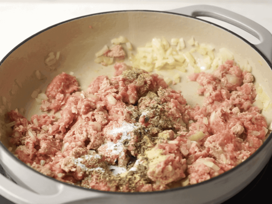 Ground turkey and yellow onions cooking in an oven safe skillet with seasonings on top