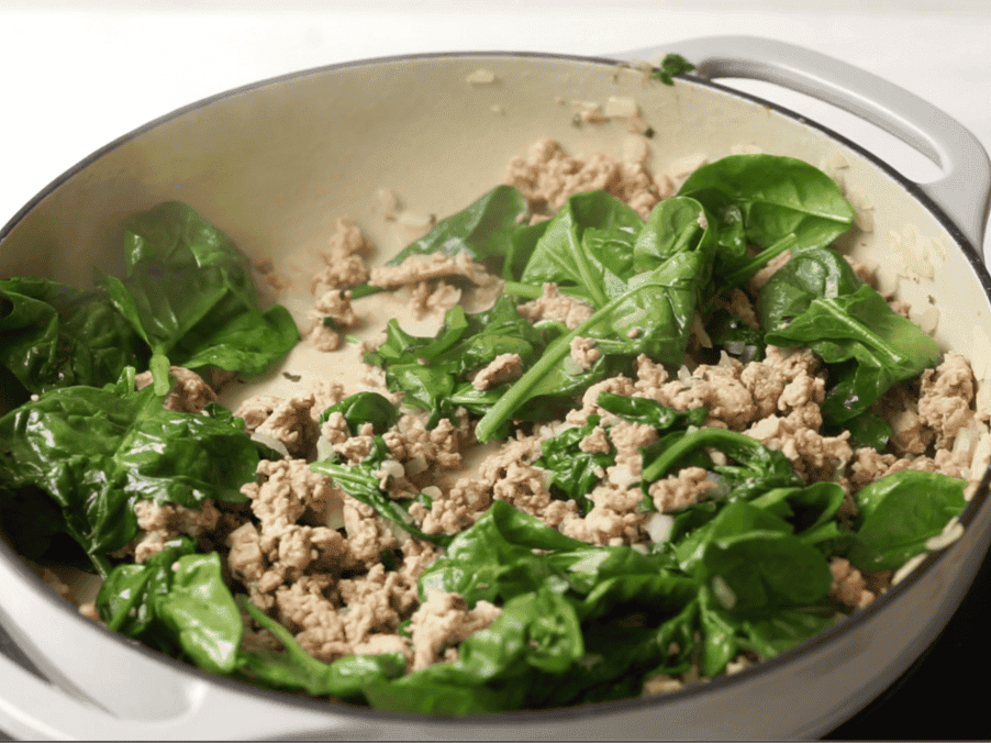 Spinach leaves, ground turkey, and yellow onions sauteeing in a large skilet