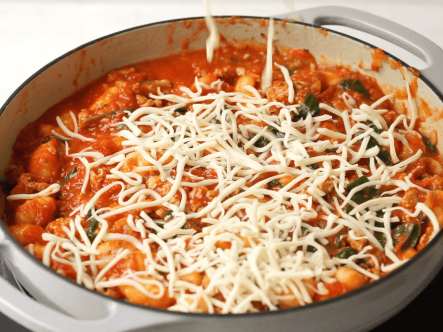 An oven safe large skillet filled with baked gnocchi ingredients including a layer of shredded mozzarella cheese on top.
