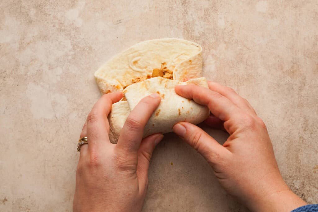 overhead shot of hands assembling a chicken burrito
