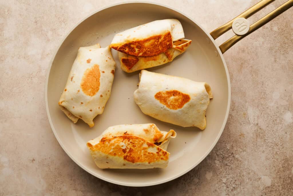 overhead shot of 4 burritos being cooked on a skillet
