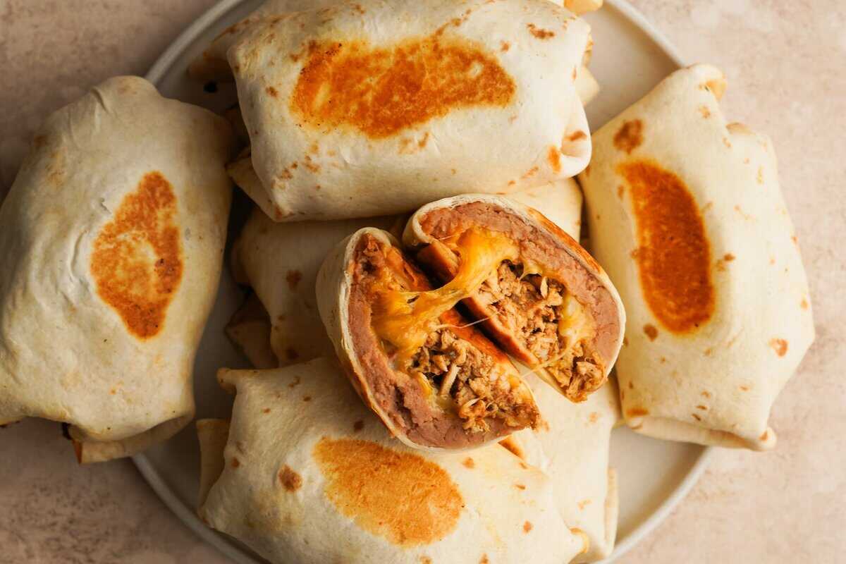 A serving plate with a stack of breakfast burritos, one on top is cut open with cheese oozing out