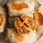 overhead shot of burritos on a plate with one cut open and cheese oozing out