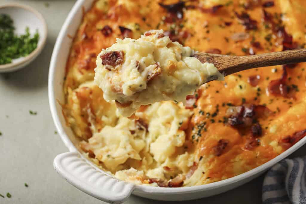 overhead shot of a cheesy twice baked potato casserole being dug into with a wooden spoon