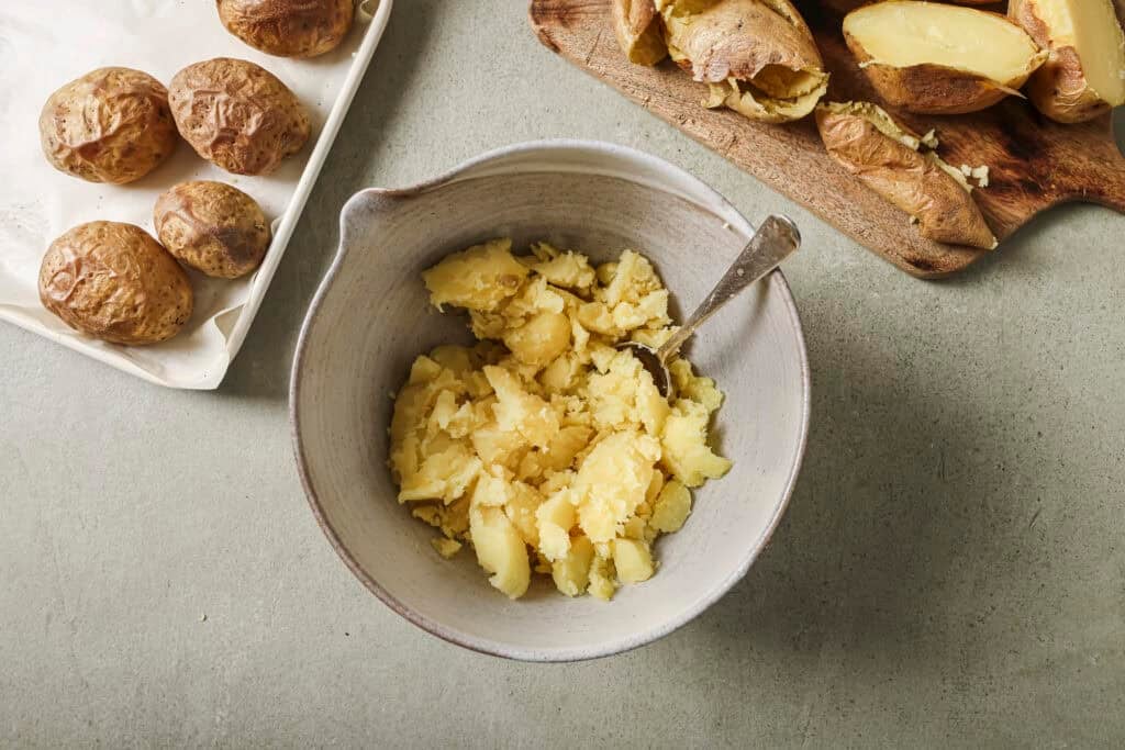 a ceramic bowl containing baked potato with other baked potatoes in the background on a baking sheet 