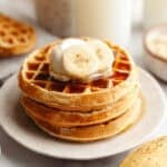 Golden brown banana bread waffles stacked one on top of another with yogurt and sliced bananas on top