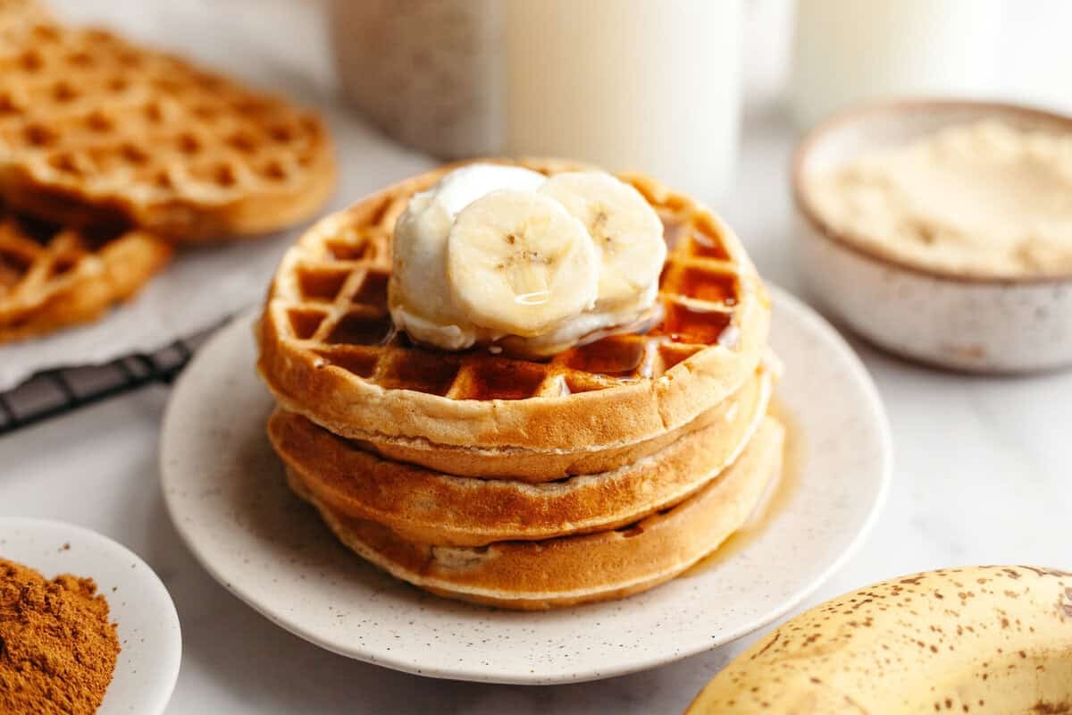 Golden brown banana bread waffles stacked one on top of another with yogurt and sliced bananas on top